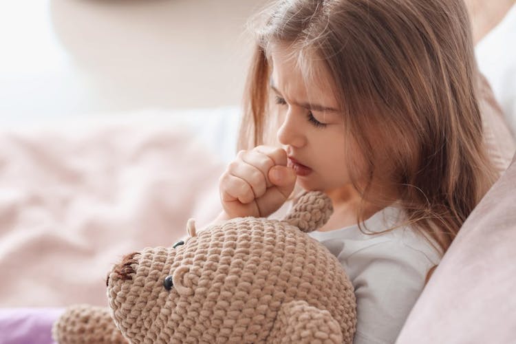 A sick girl holding a teddy bear and coughing