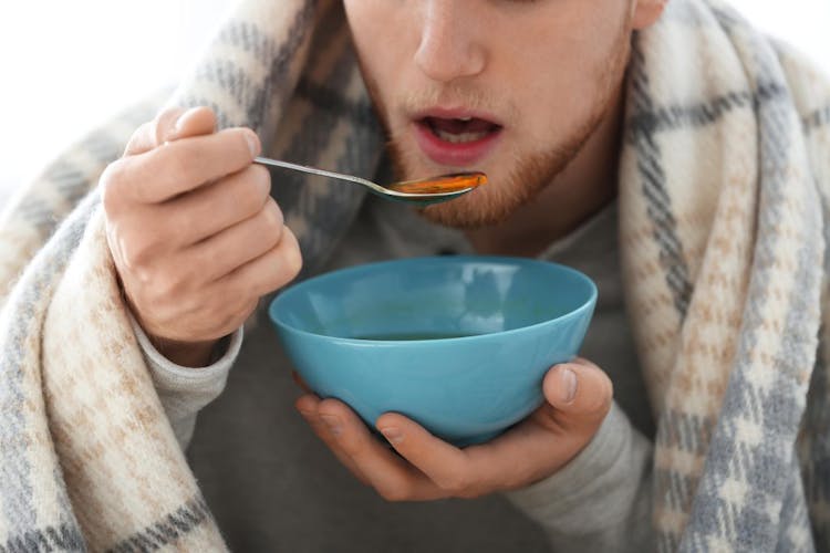 A man staying warm by eating soup and covering up with a blanket over his shoulders