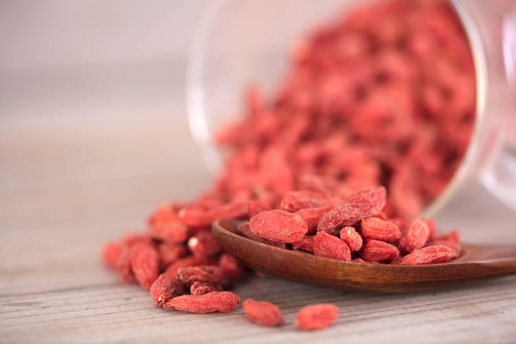 Red goji berries falling out of a clear container onto a brown wooden spoon