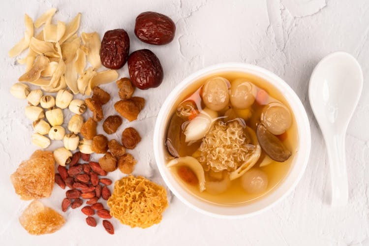 TCM herbal soup in a white bowl pictured next to herbal soup ingredients such as goji berries, red Chinese dates, and snow fungus 
