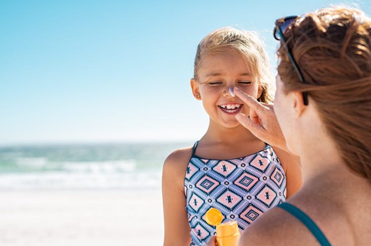 A mom applying sunscreen to her daughter's nose while at the beach