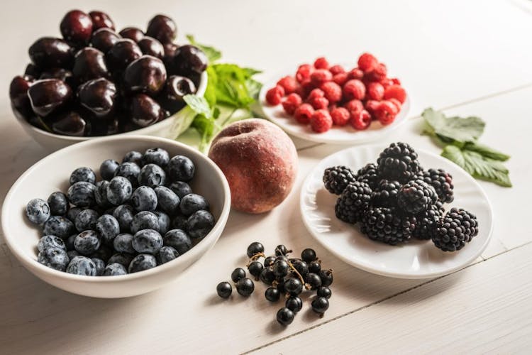 High antioxidant foods such as blackberries, blueberries, cherries, and raspberries pictured on white plates 
