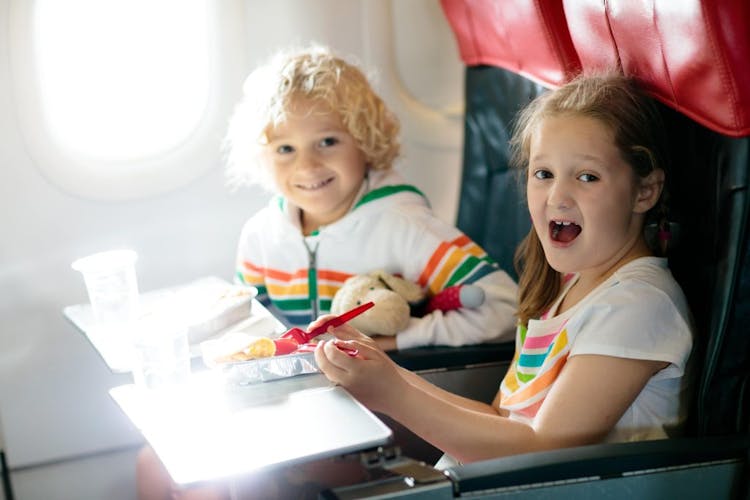 Two children sitting in their seats on an airplane eating healthy snacks