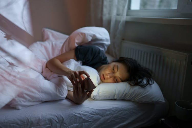 A woman lying in bed scrolling through her phone at night