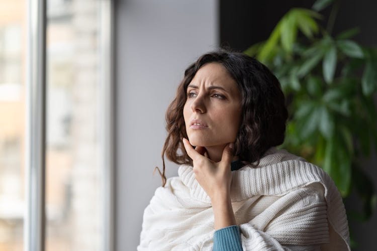 A woman in a sweater feeling her swollen lymph nodes