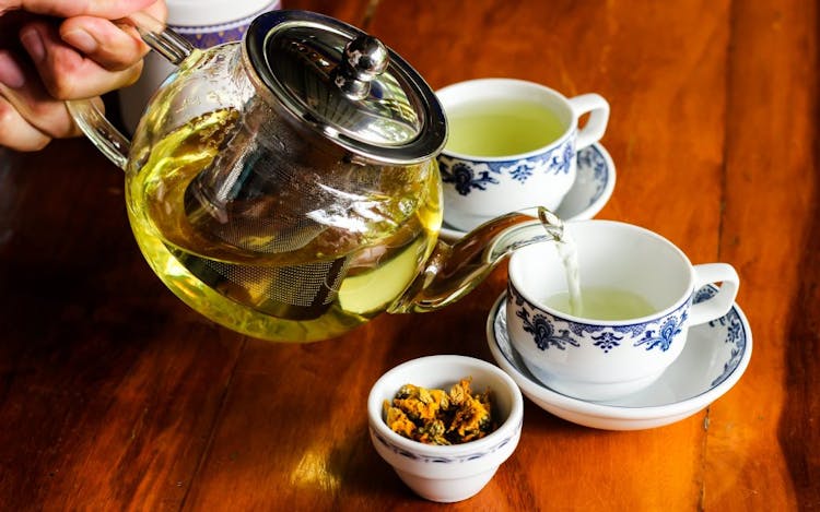 An image of dried chrysanthemum flower buds and white chrysanthemum tea being poured from a teapot into teacups 