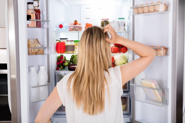 A woman standing in front of her refrigerator looking for something to eat