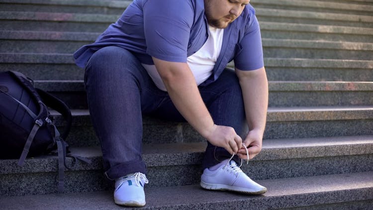 An obese man struggling to tie his shoes 