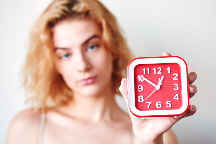 A unhappy looking young woman holding a clock