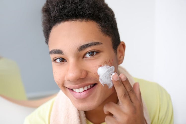 A teenage boy with acne applying moisturizer to his face