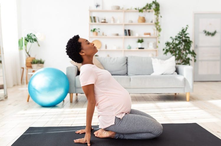 A pregnant woman stretching on a yoga mat with an exercise ball in the background