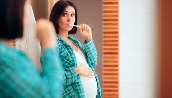 Pregnant woman brushing her teeth min scaled