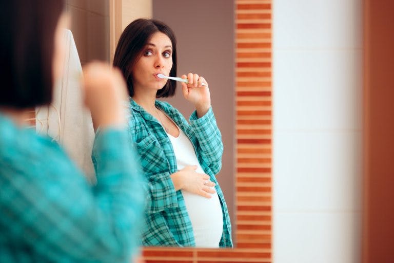 Pregnant woman brushing her teeth min scaled
