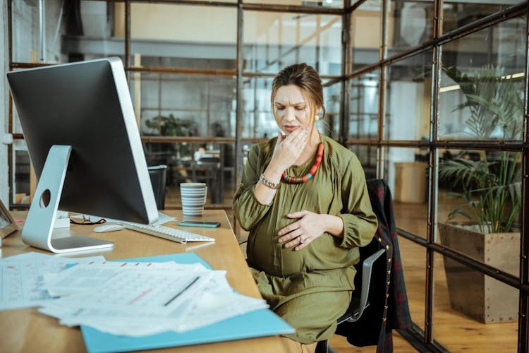 A pregnant woman with a toothache sitting at her work desk