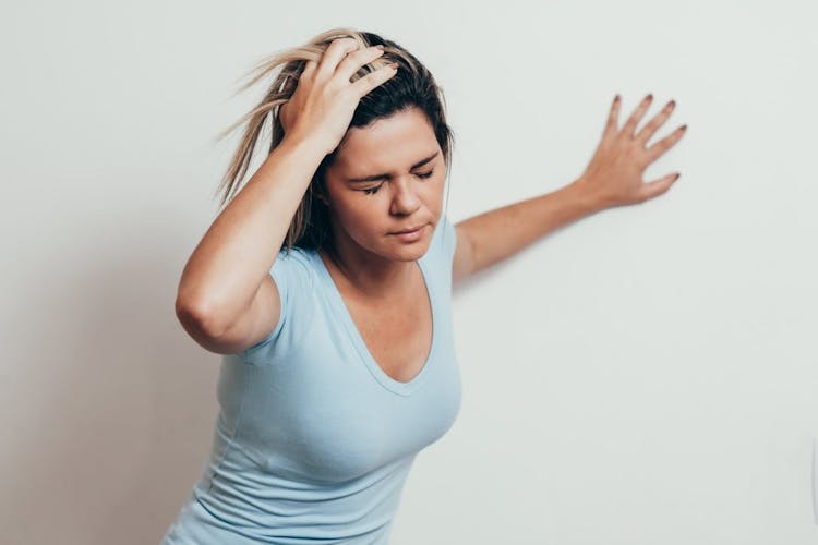A young woman experiencing dizziness and embracing the wall for balance 