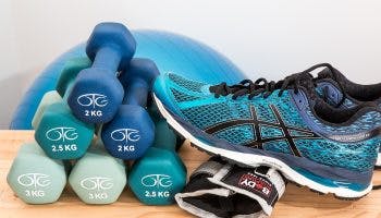 Sports shoes and gloves next to blue dumbbells and a medicine ball.