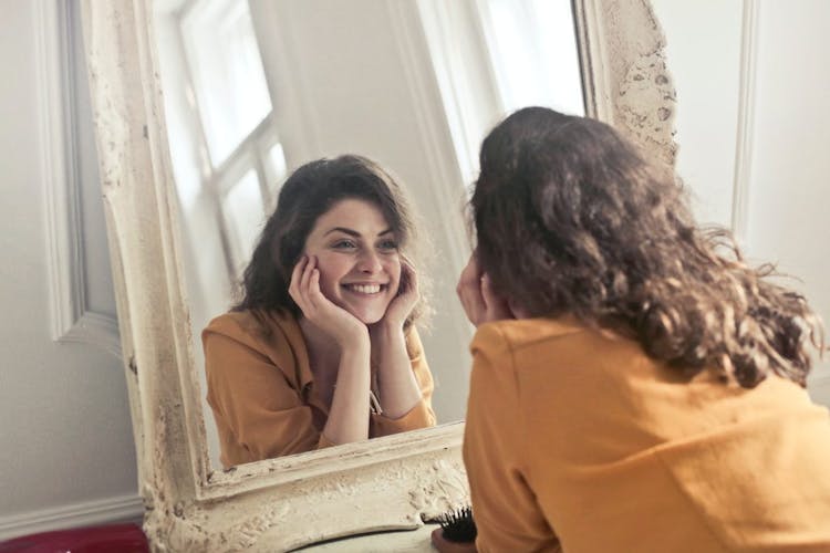 A lady looking into the mirror and smiling to herself