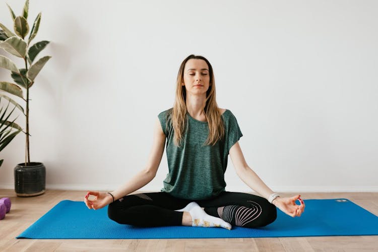 A lady doing meditation on a blue yoga mat