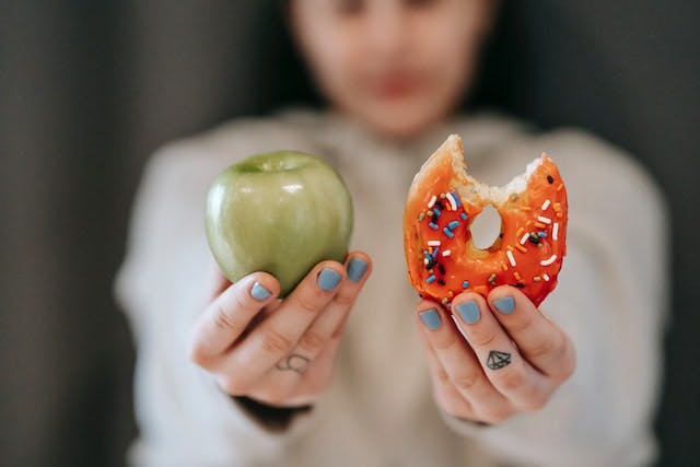 Person holding an apple and a doughnut.