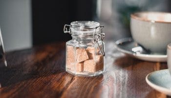 Clear condiment shaker with brown sugar cubes near gray teacup.