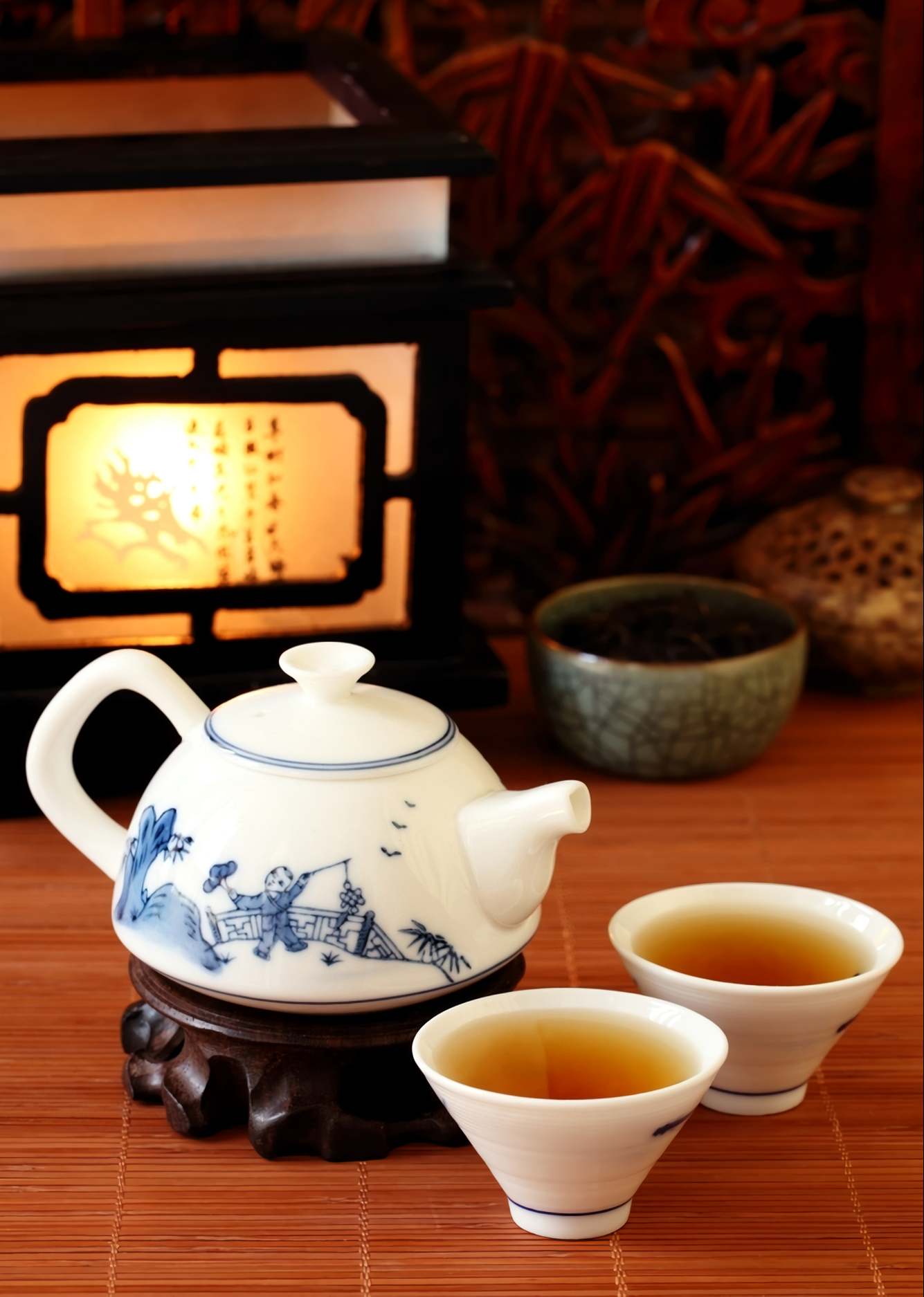 chinese styled white teapot and two tea cups with traditional chinese lamp on brown table