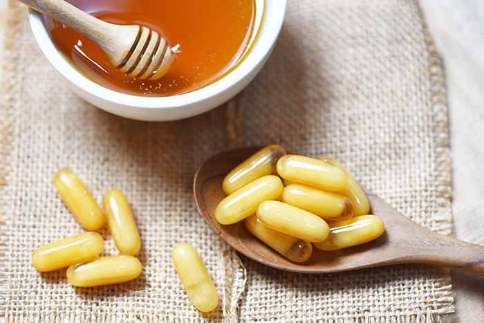 Royal jelly capsules in wooden spoon on sack background