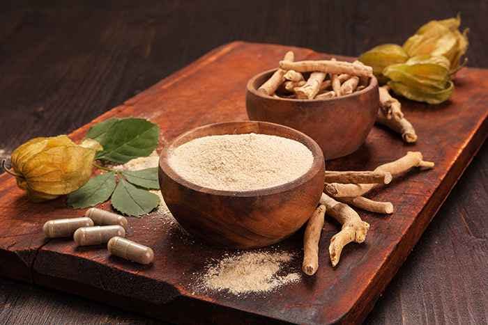 A display of ashwagandha leaves, pills, powder and roots in wooden bowls on a wooden tray