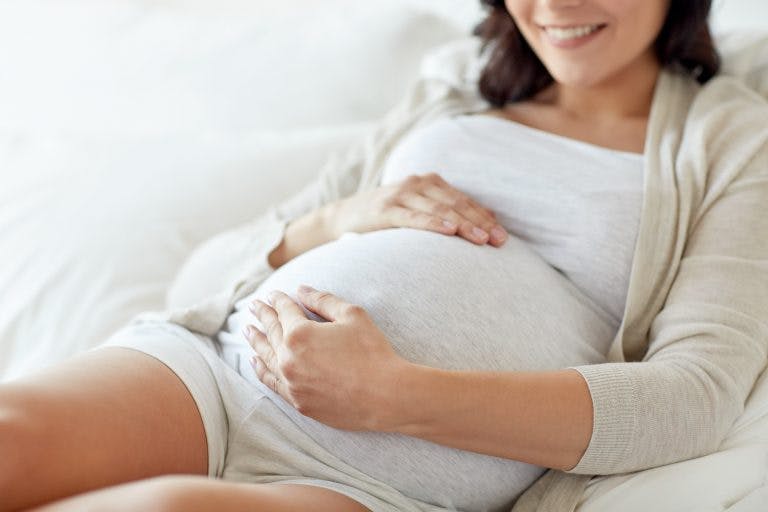 A pregnant woman holding her belly while sitting on a white bed