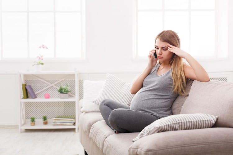 A pregnant woman with her smartphone, sitting on a sofa