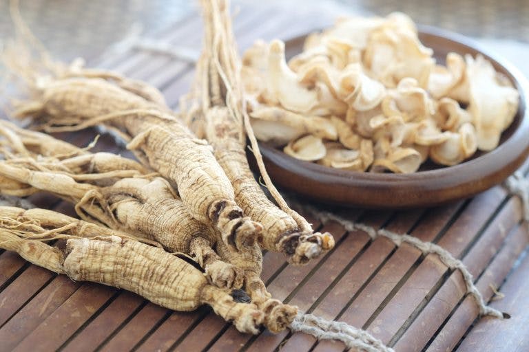 Ginseng roots on a bamboo mat with sliced american ginger roots in a wooden bowl