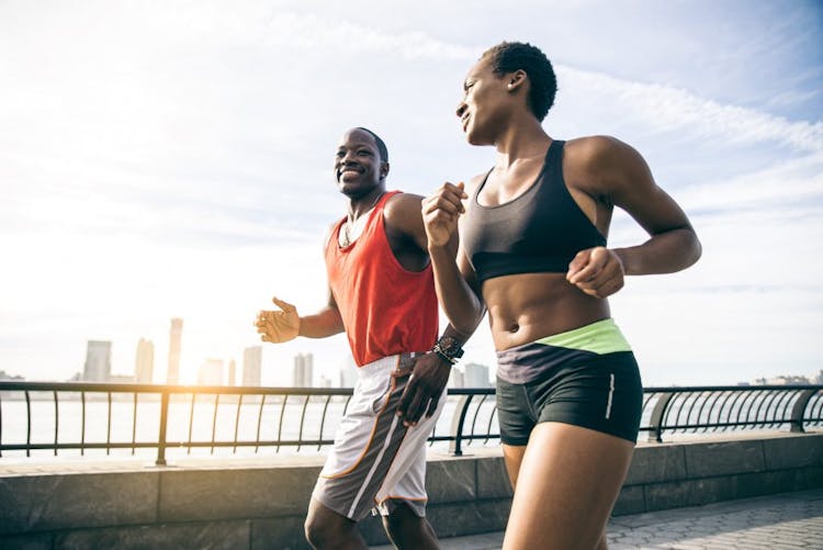 A black couple running together wearing gym clothes, outside the city