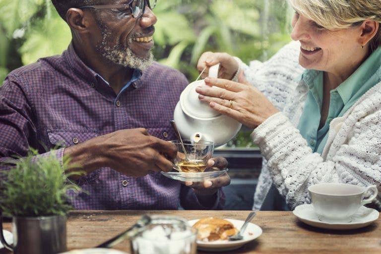A white senior woman pouring tea in a glass for a black senior man
