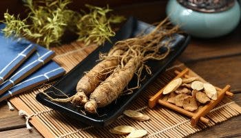 Two asian ginseng roots on a black modern plate placed on top of a bamboo mat