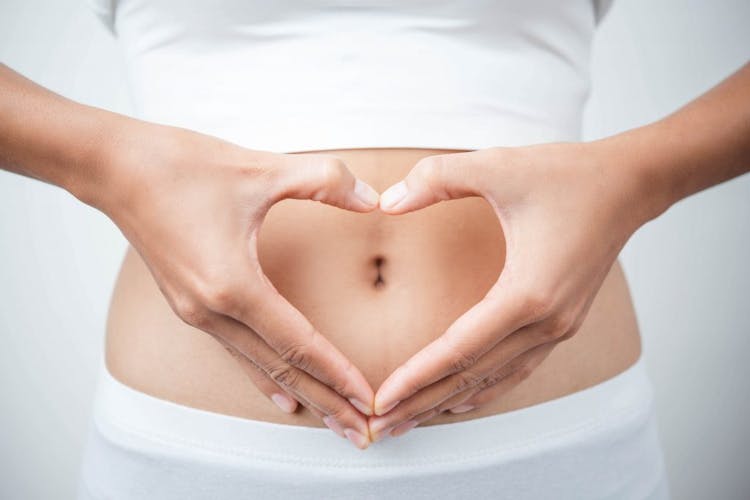 A pair of female hands in the shape of a heart is placed on top of her stomach