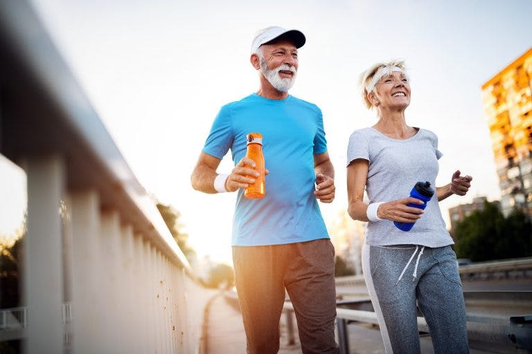 Mature couple jogging and running outdoors in city holding water bottles