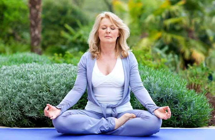 A woman meditating on a yoga mat in her garden