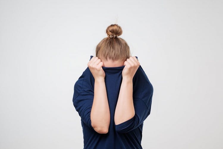A woman covering her face with her blue sweater