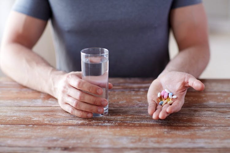 A man holding medication for bipolar disorder and a glass of water.