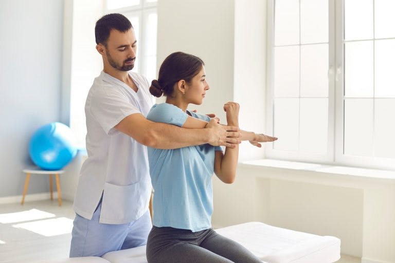A man chiropractor or physician helps woman stretch her muscles to relieve muscle tension
