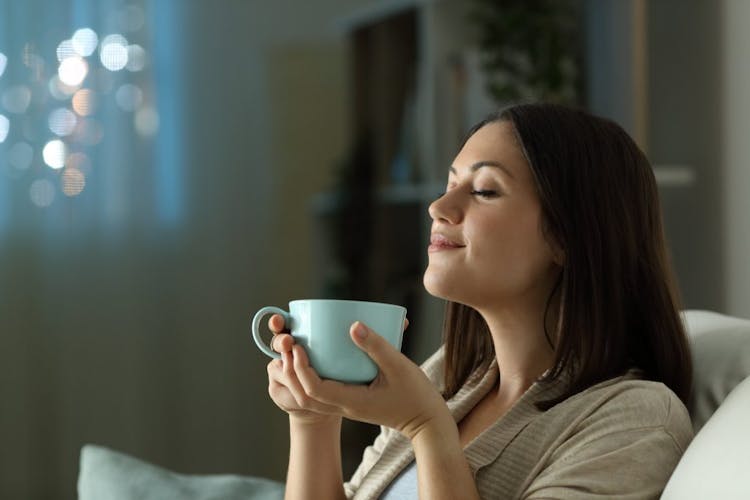 A woman drinking a cup of tea at night in the living room