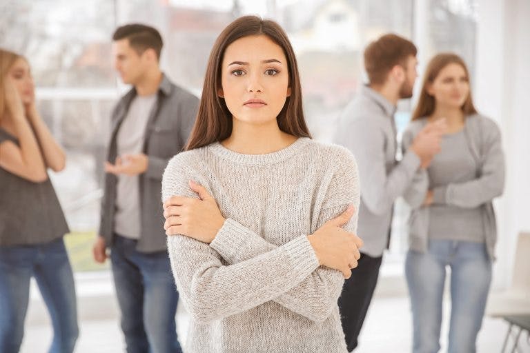 An anxious woman wearing grey sweater stand alone in a crowd