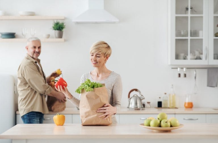 a young woman and a senior man unloading groceries filled with anti aging foods in the kitchen