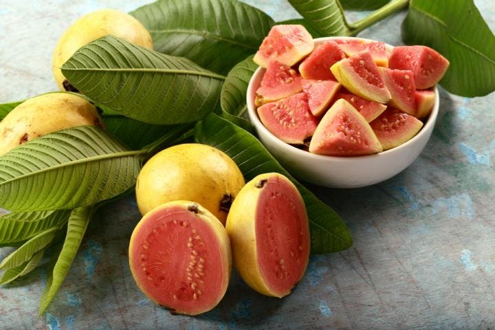 Slices of fresh guava in a bowl and on a concrete tabletop with guava leaves
