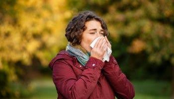 A woman sneezes on a tissue as she is experiencing flu symptoms outdoor