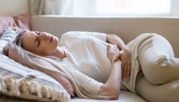 A white woman lying on the bed while holding her stomach in pain due to digestive problems