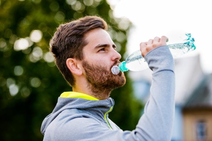 A young white male drinking a bottled water during workout