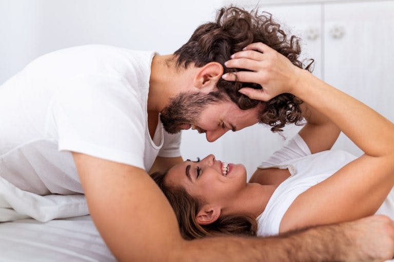 A happy man and woman cuddling on the bed wearing white shirts