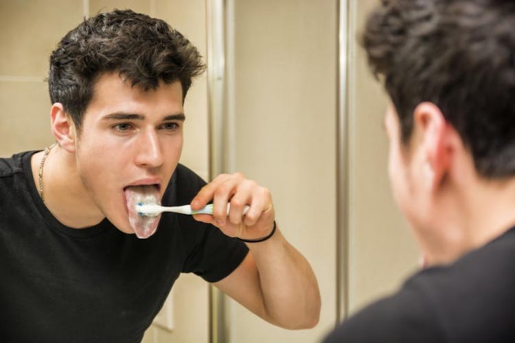 A man cleaning his tongue with toothbrush and toothpaste in the bathroom