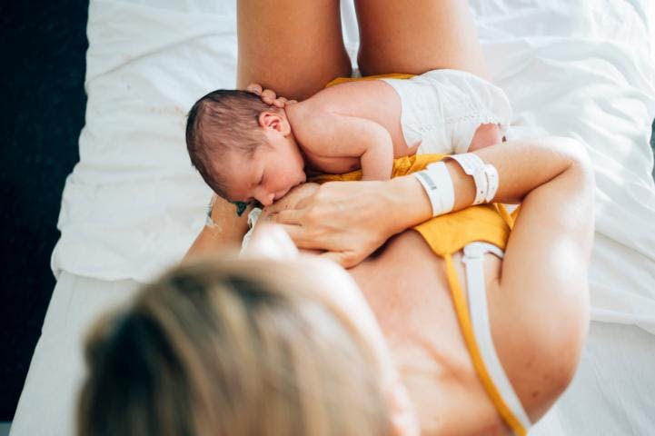 A mother in yellow top breastfeeding her newborn baby on a bed