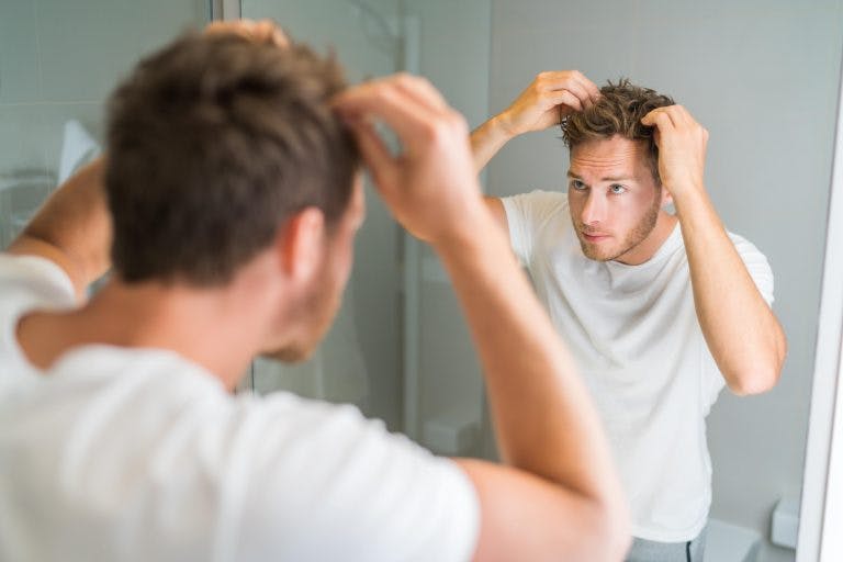 A young Caucasian man touching his hair in front of the mirror
